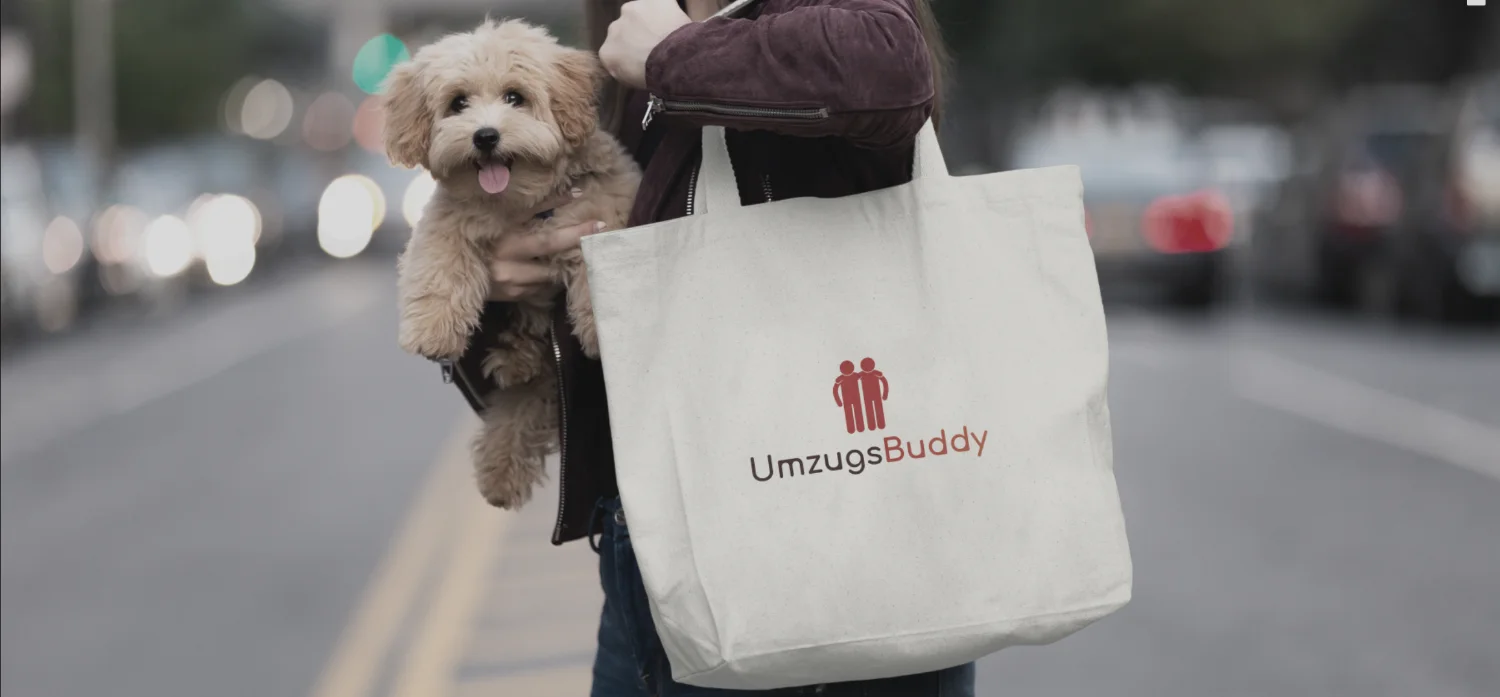 Das Logo von UmzugsBuddy in Rot auf einer getragenen Baumwolltasche, im Hintergrund eine Straße